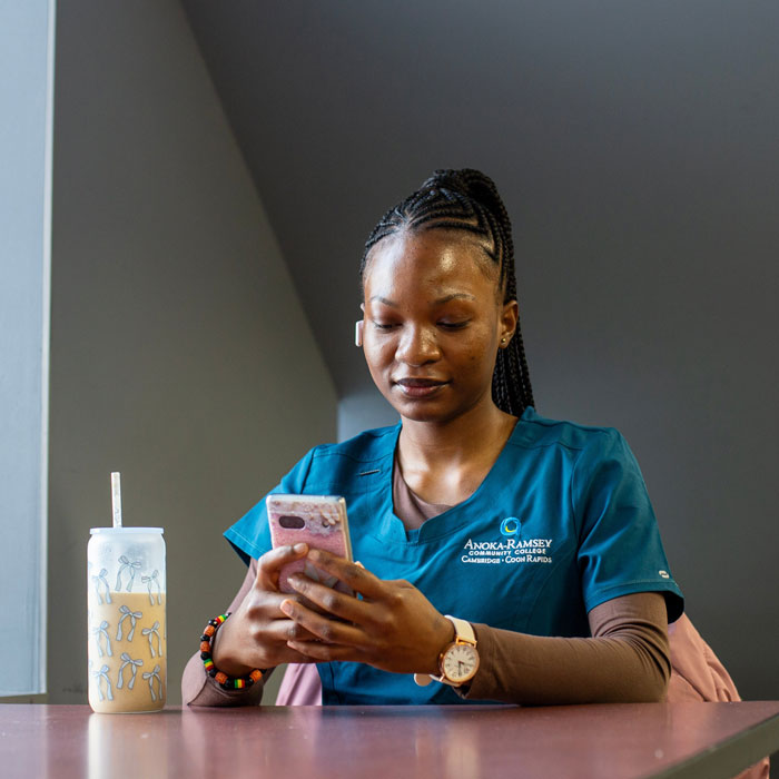 student in scrub shirt with college logo sitting holding phone