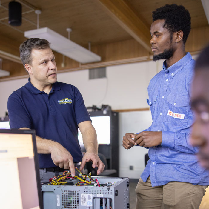 Two people in a computer lab work on a desktop PC during hands-on technical training.