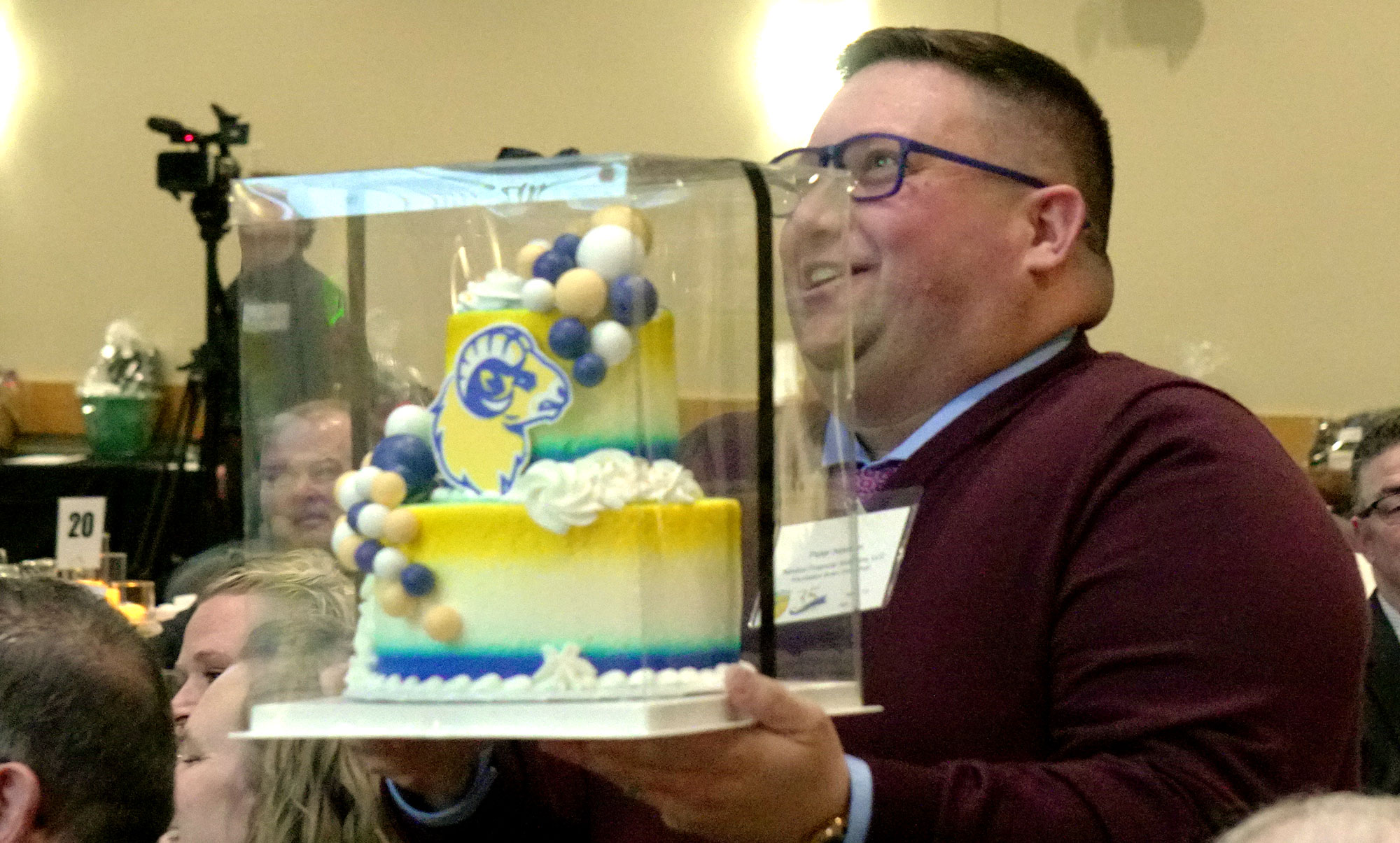 Smiling Man Carrying Cake with Anoka-Ramsey Ram Logo it