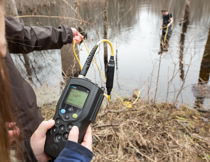 Students measuring water quality with handheld equipment at a pond.