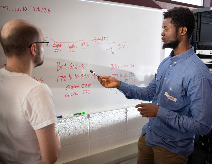 Instructor and student at a whiteboard discussing a computer networking issue