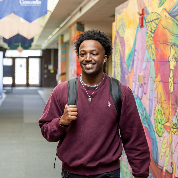 Student with backpack walking through a campus hallway with a colorful mural.