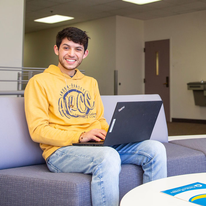 smiling student in yellow arcc sweatshirt seated with laptop on campus