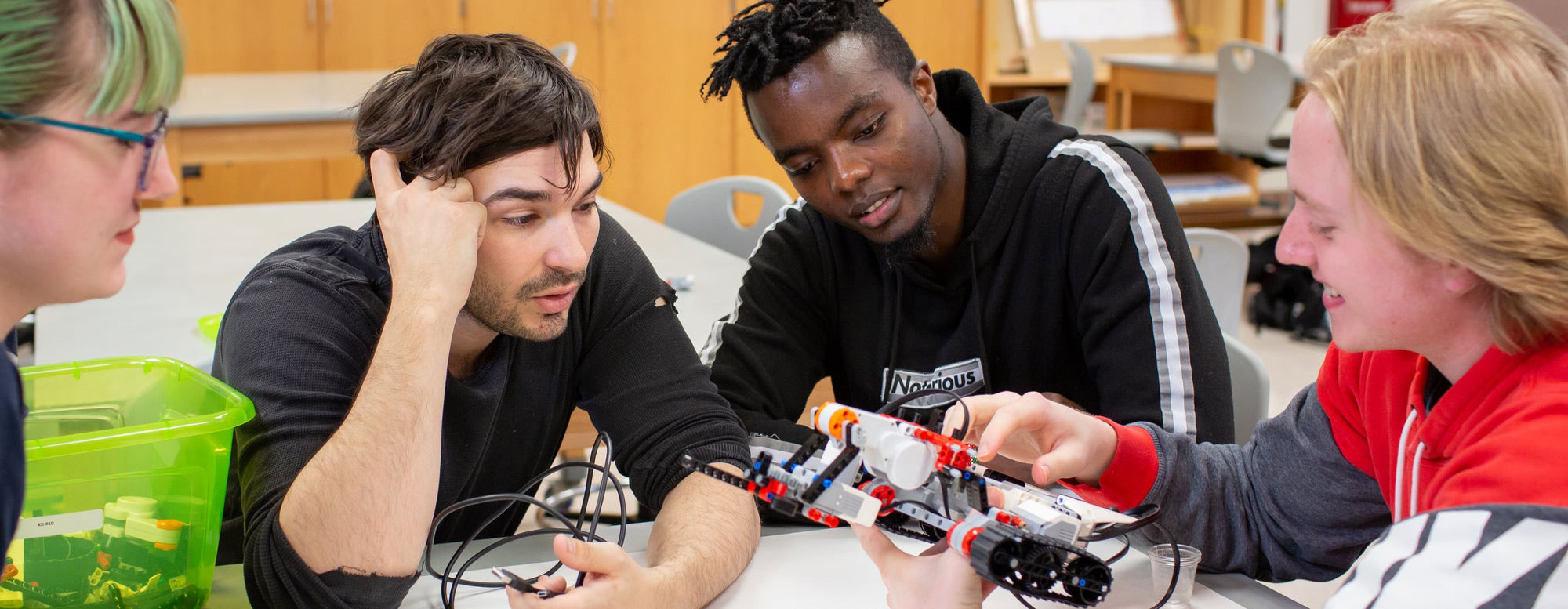 Students collaborating at a table while building and examining a small robotic device.
