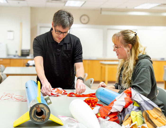 Two people working at a table on a model rocket project in a classroom lab.