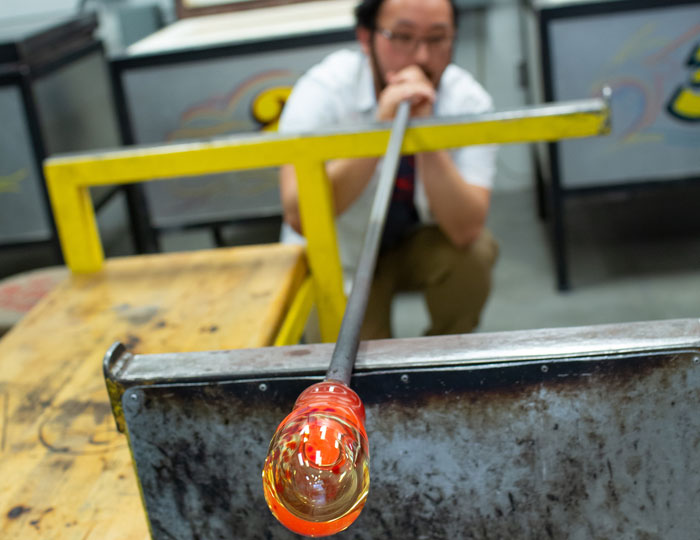 Close-up of molten glass on a blowpipe as a student shapes it at a workstation in anoka-ramsey's glass‑blowing studio.