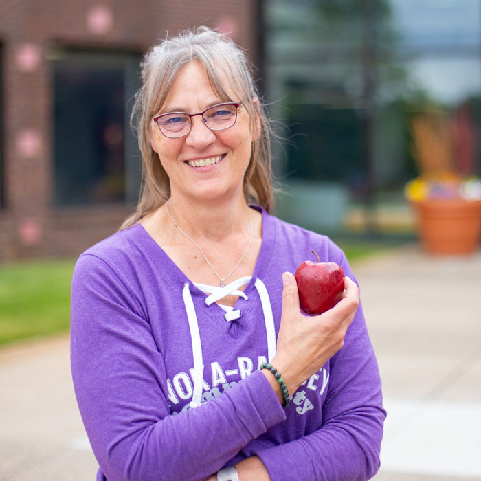 Person standing outdoors holding a red apple.