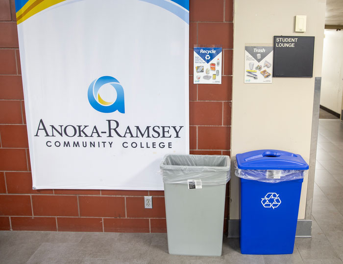 Recycling station next to Anoka Ramsey banner inside building hallway
