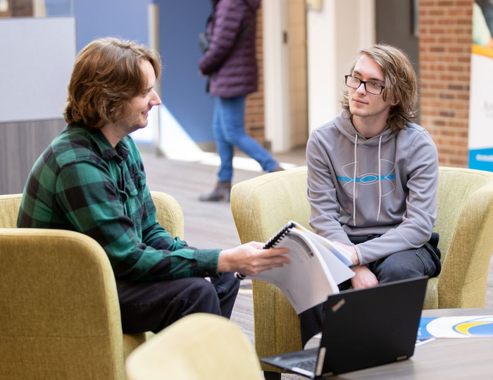 two men sitting across from each other discussing a packet of information