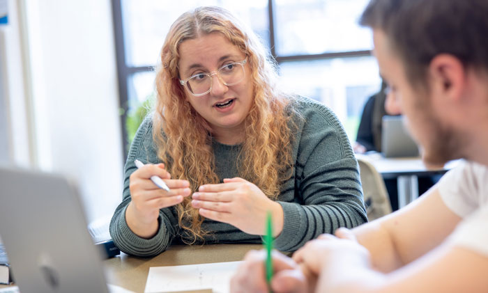 Students discuss coursework at a table with laptop and notes