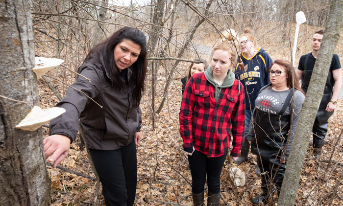 Instructor points to fungi on a tree during an outdoor class with students.