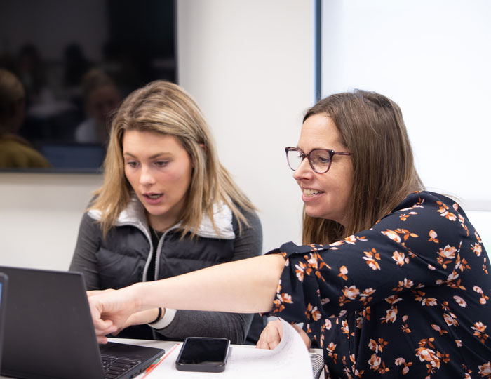 Two people review work on a laptop during a classroom meeting