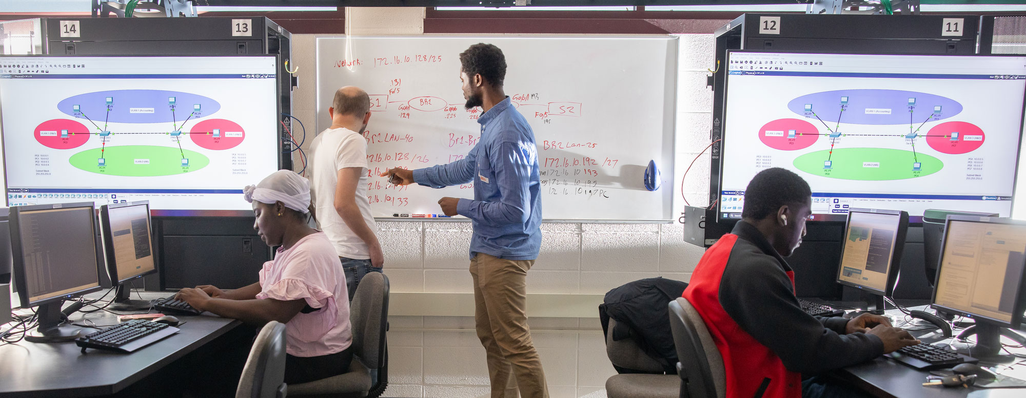 four students and instructors in IT classroom working at whiteboard and computers