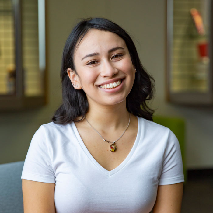 Portrait of person wearing a white V-neck shirt indoors with a softly blurred background.
