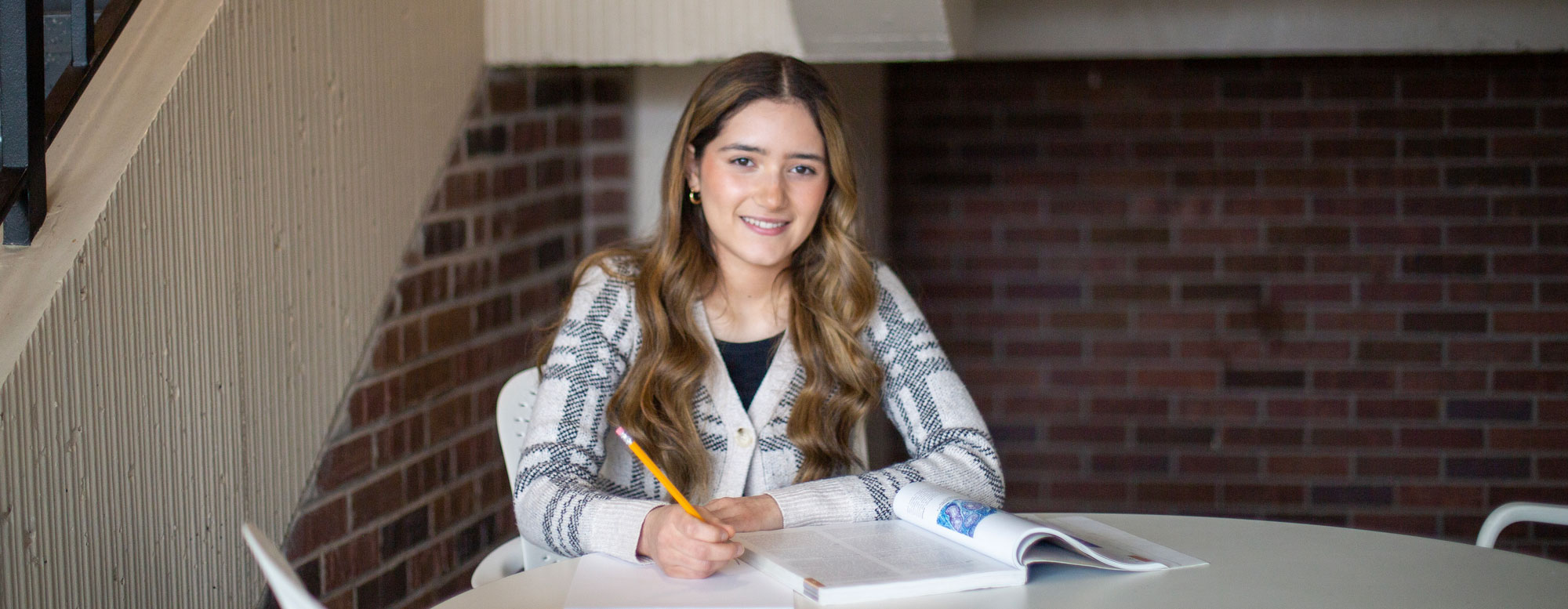 female student at table taking notes from textbook