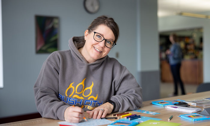Student sitting at a table on campus completing paperwork and using colored pencils with school supplies spread out.