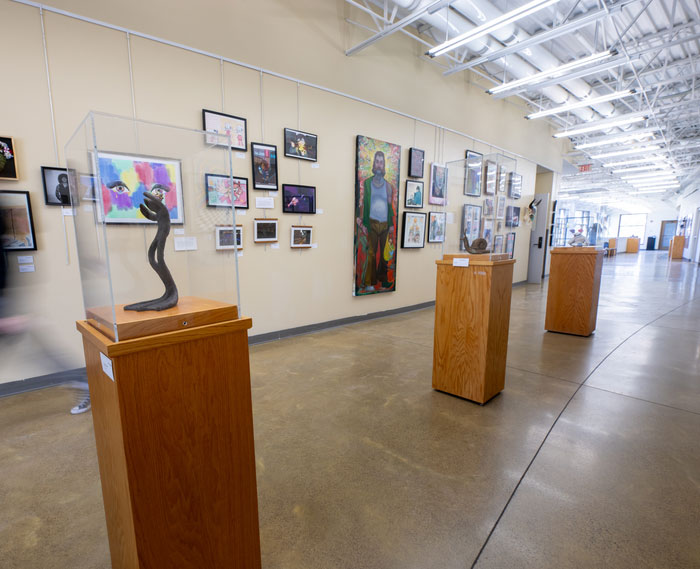 Student artwork displayed in a campus visual arts gallery, featuring sculptures and framed pieces exhibited in a college art and design center.