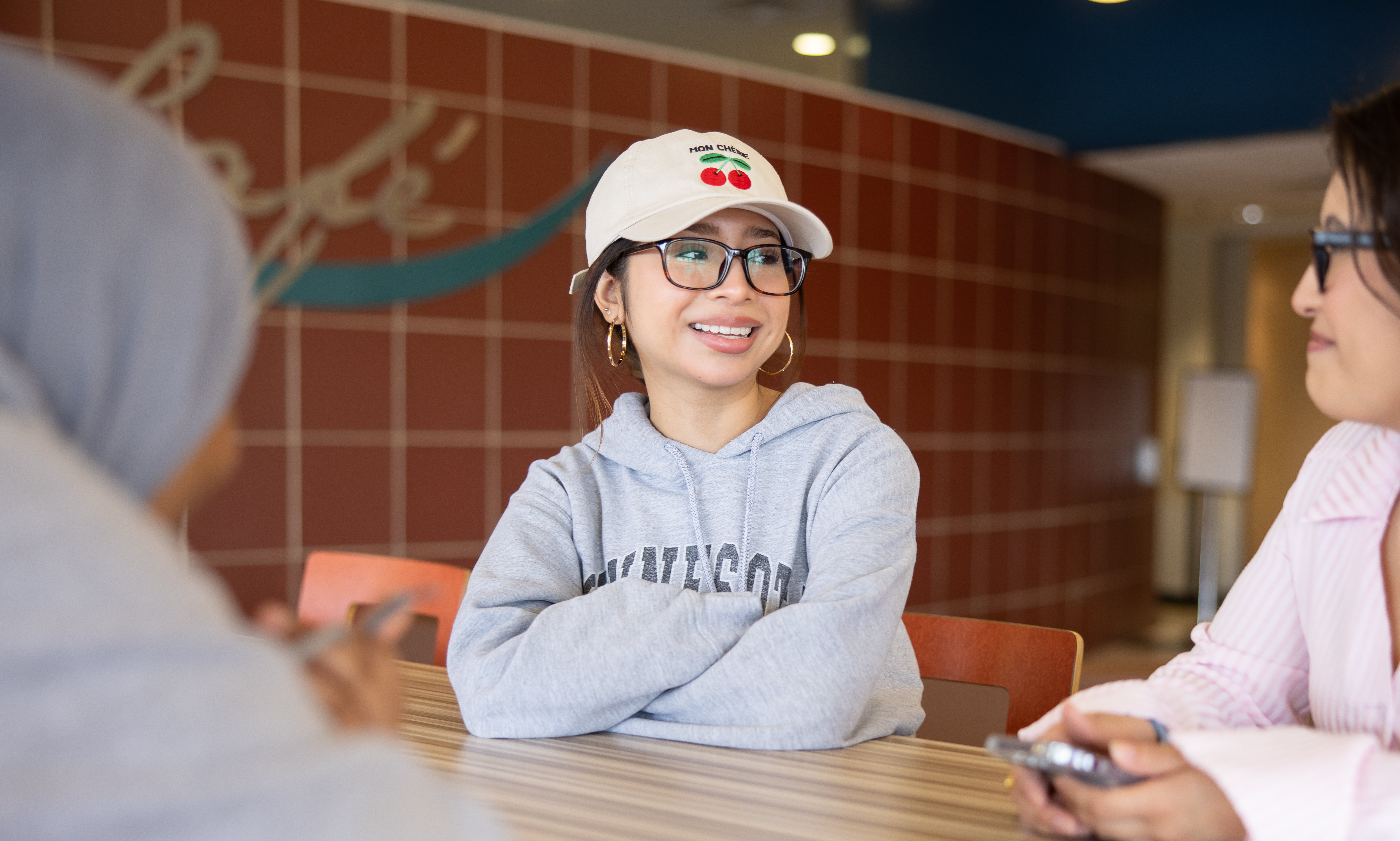a women sitting at a high top table in the café with her arms crossed smiling at another student