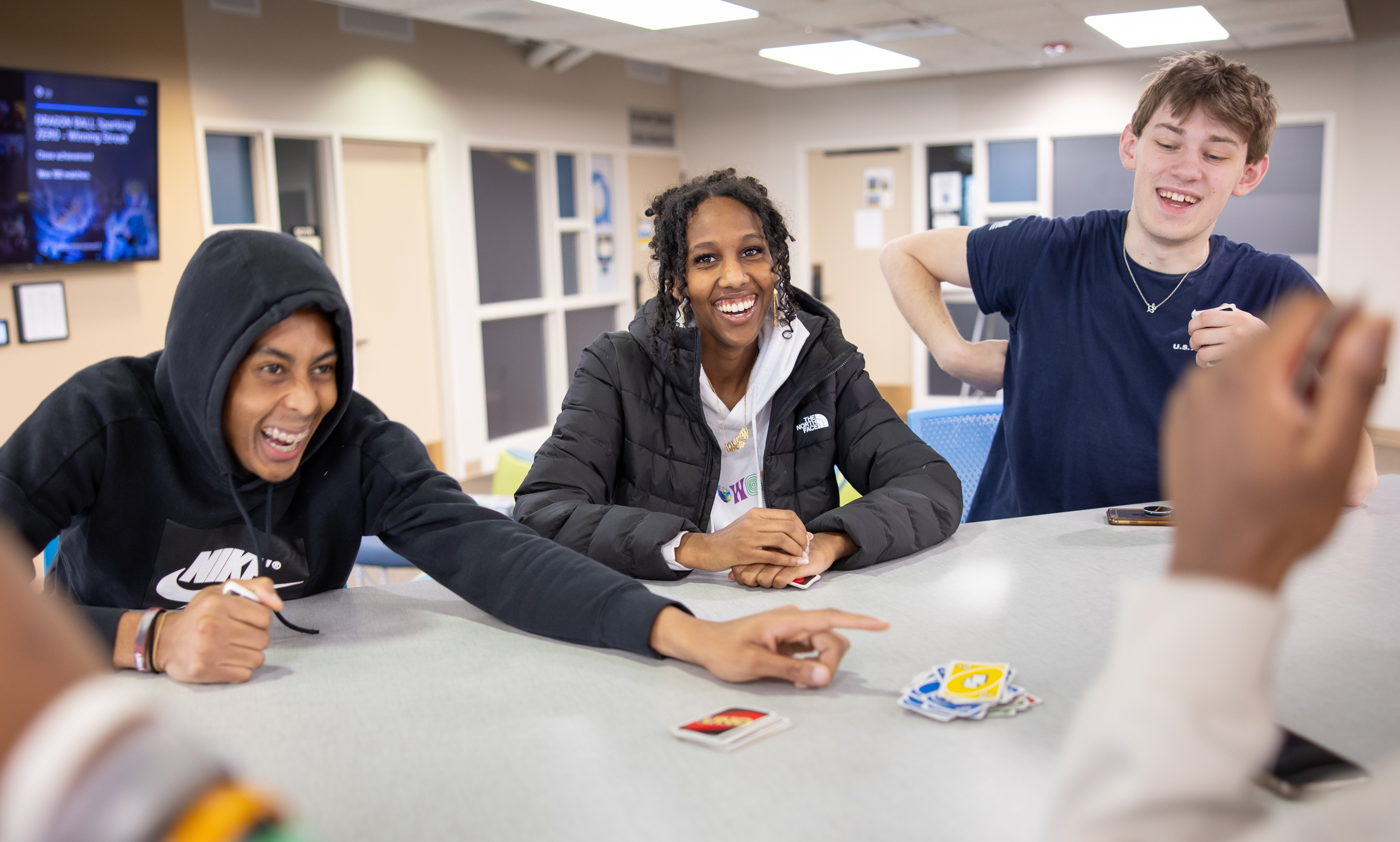 a group of students sitting around a table smiling while playing a game of cards