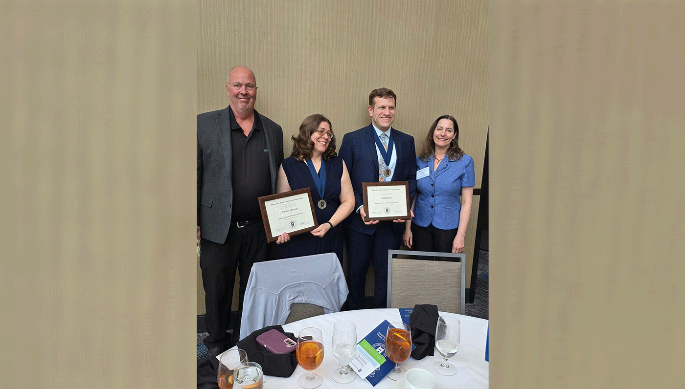 Four individuals standing near table, two holding awards. 