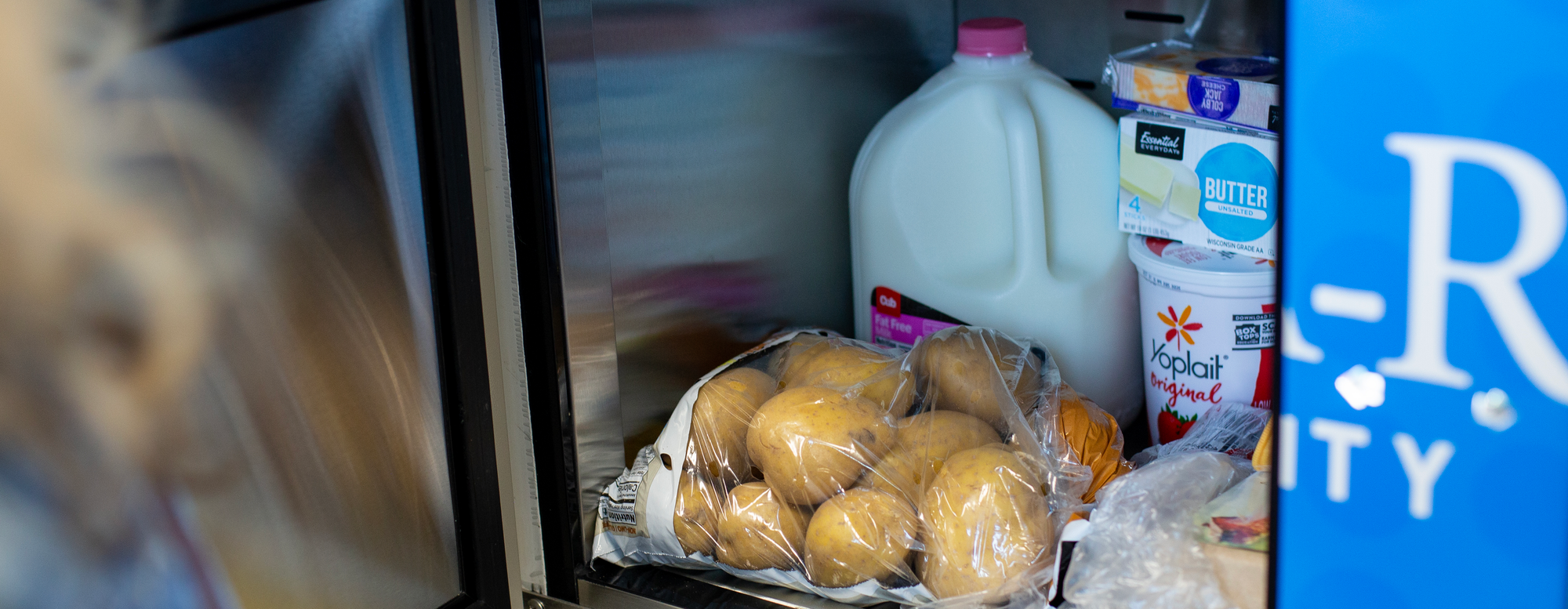 Interior of food locker containing jug of milk, bag of potatoes and other assorted food items.