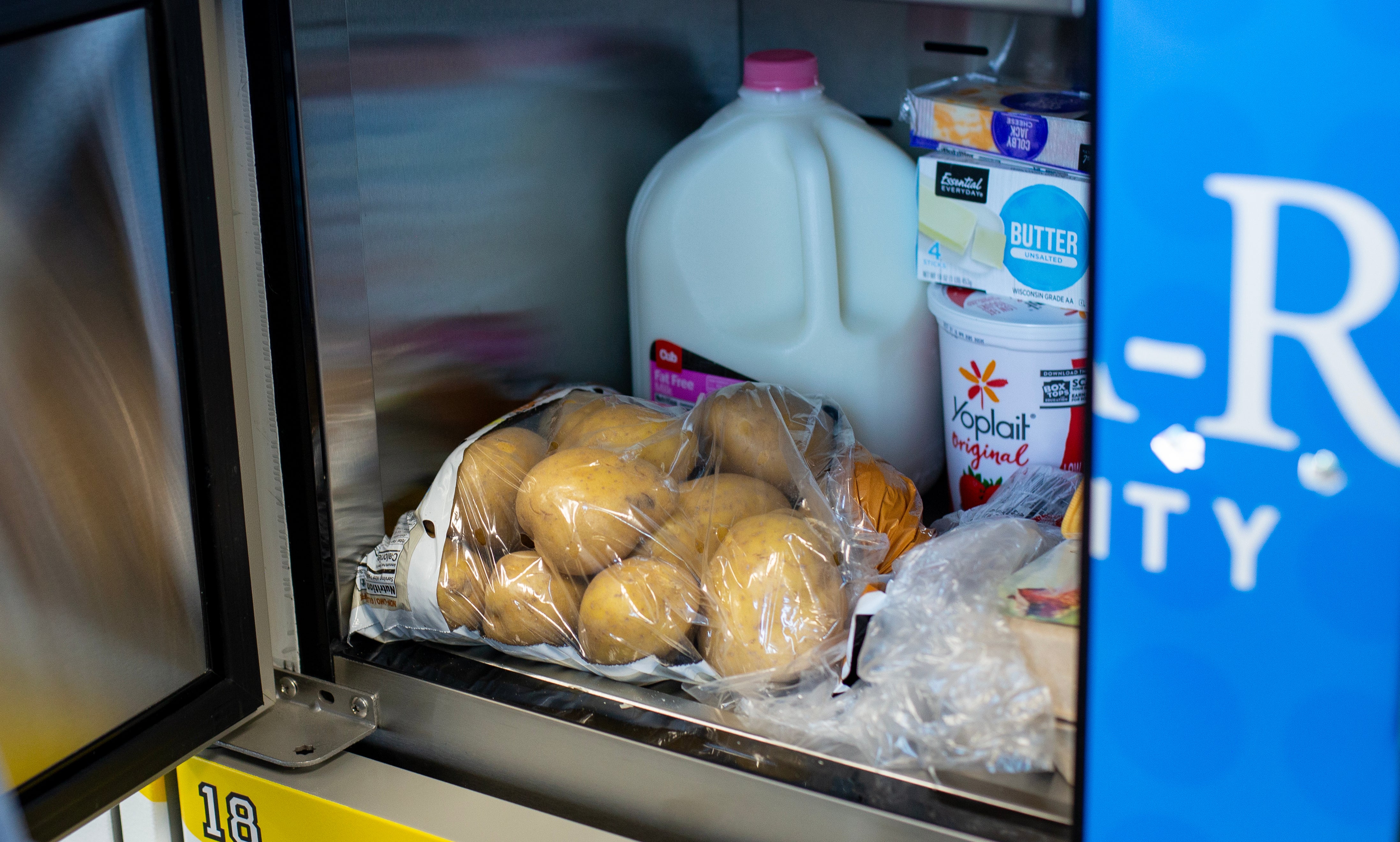 Inside a refrigerated food storage container showing a bag of potatoes, milk, yogurt, butter and a block of cheese.
